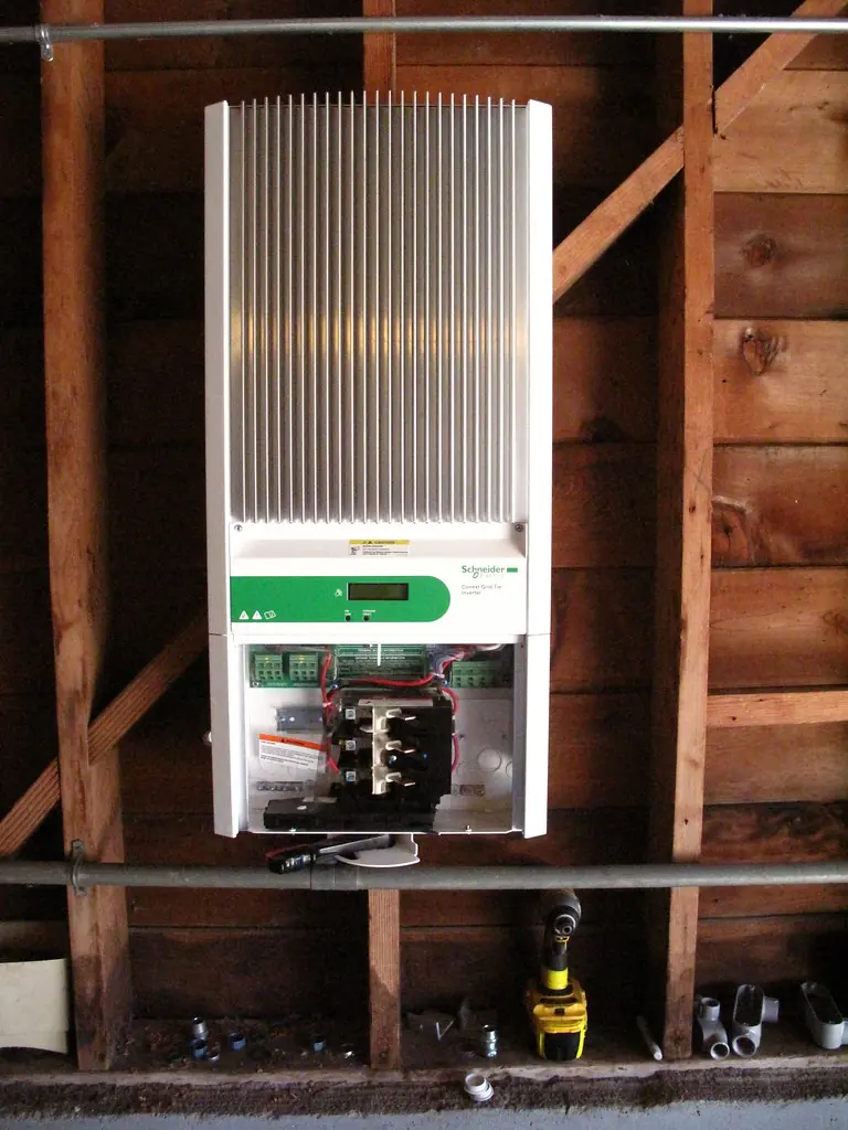 A wall mounted solar inverter with the cover open inside a timber building